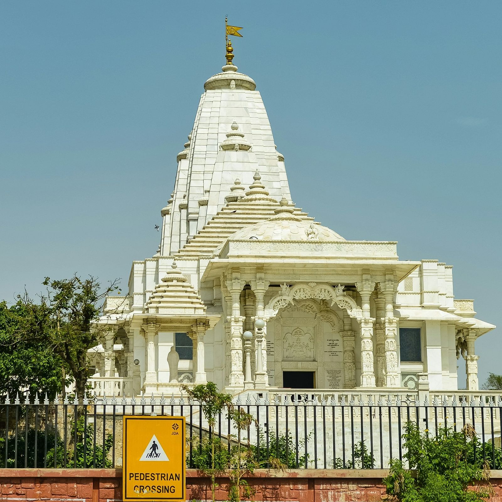 A white temple against a clear sky, surrounded by trees and plants.